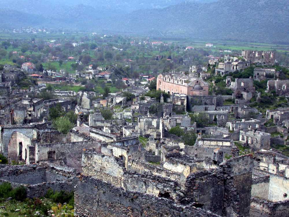 The abandoned stone houses of Karmylassos Ancient City (Kayaköy) leaning against the hillside and the remains of Taksiyarhis Church rising in the silhouette.